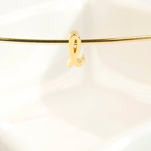 May include: A gold-colored letter L charm hangs from a thin gold-colored chain.