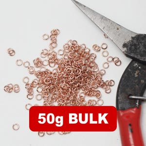 Op de afbeelding: Een verzameling koperkleurige sprongringen verspreid op een witte ondergrond, met een tang op de achtergrond. Een rode rechthoek met de tekst "50g BULK" staat onderaan. Ideaal voor het maken van sieraden en knutselen.