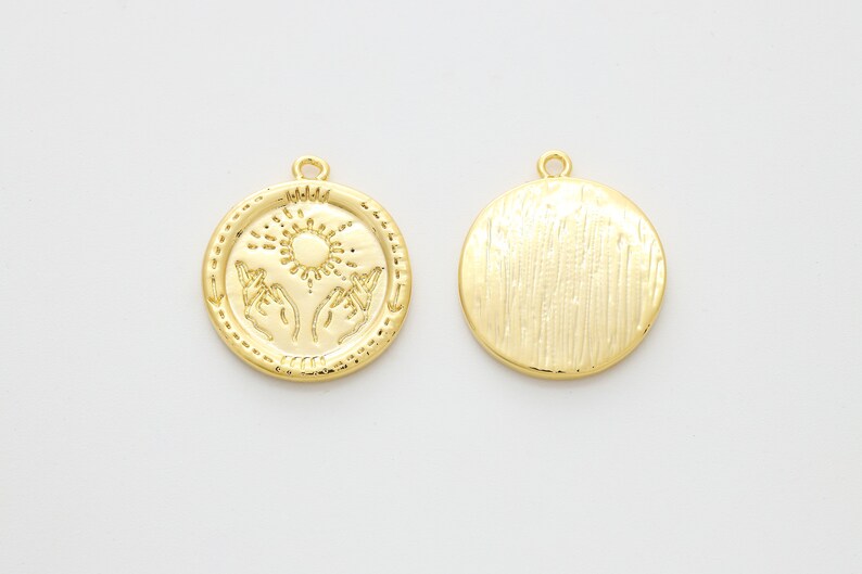 May include: Gold-toned metal pendant charm with a sun and two hands design on one side and a textured surface on the other side.
