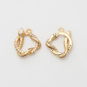 Può includere: Due ciondoli a forma di serpente color oro. Un ciondolo è incastonato con piccoli cristalli trasparenti. Entrambi i ciondoli hanno un anello nella parte superiore per il fissaggio ai gioielli. Su sfondo bianco.