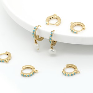 Puede incluir: Cinco pendientes de aro dorados con piedras turquesa. Dos de los pendientes tienen un dije de perla colgando.