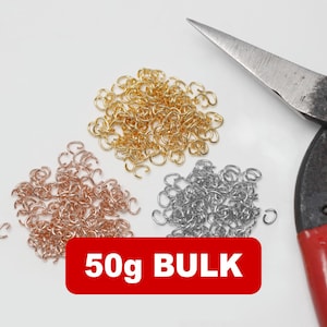 Op de afbeelding: Drie stapels metalen sprongringen in goud, koper en zilver. Een metalen schaar met rode handvatten staat op de achtergrond. Een rode rechthoek met de tekst "50g BULK" staat onderaan.