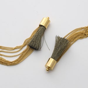 May include: Two gold chain tassel earrings with black and gold fringe. The tassels are attached to a gold metal cap.