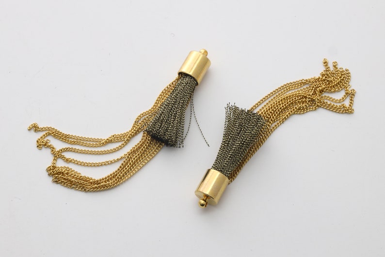 May include: Two gold chain tassel earrings with black and gold fringe. The tassels are attached to a gold metal cap.
