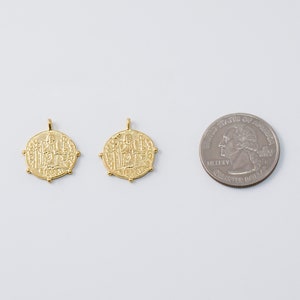May include: Two gold-toned pendants with intricate designs, each featuring a central figure surrounded by smaller figures. The pendants are about the size of a US quarter.