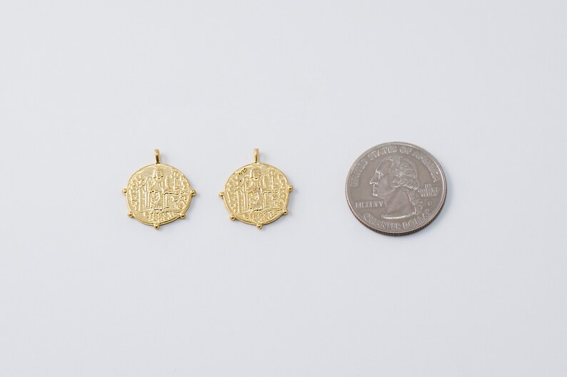 May include: Two gold-toned pendants with intricate designs, each featuring a central figure surrounded by smaller figures. The pendants are about the size of a US quarter.