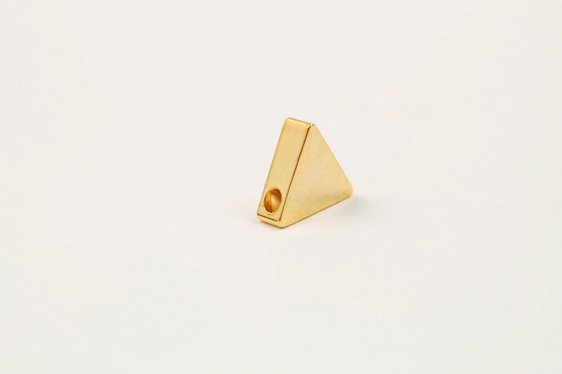 May include: A gold triangle-shaped pendant with a hole in the centre for stringing.