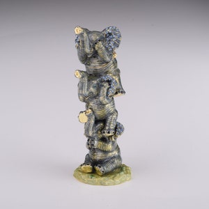 May include: A stack of four gray ceramic elephants with blue accents. The elephants are stacked on top of each other, with the largest elephant at the bottom and the smallest elephant at the top. The elephants are all facing forward, and their trunks are raised.