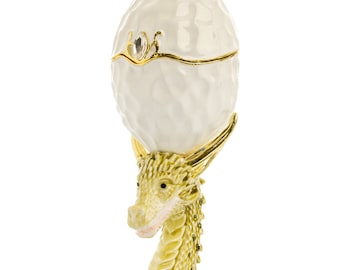May include: A gold dragon figurine holding a white porcelain egg with a gold lid and a crystal accent. The dragon is standing on a bed of gold crystals.
