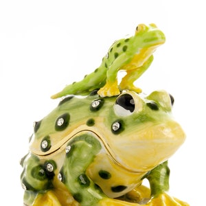 May include: A yellow and green frog figurine with a smaller green frog figurine on top. Both frogs are decorated with rhinestones.