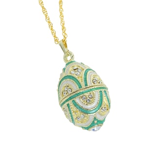 May include: A gold-toned necklace with an egg-shaped pendant. The pendant is decorated with white, green, and gold enamel, and adorned with small, clear crystals. The necklace has a delicate chain.