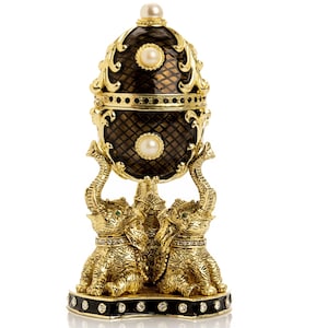 May include: A decorative egg-shaped trinket box. The black and gold box is supported by three gold elephants. The egg has a pearl on top and two more pearls on the front. The base is black with small crystals.