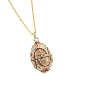 May include: A gold-toned necklace with a pendant shaped like an egg. The egg pendant is decorated with red, peach, and gold enamel, and embellished with clear crystals. The chain is a delicate, twisted design.