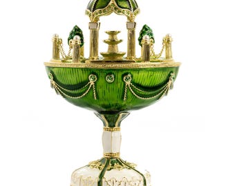 May include: A decorative, ornate chalice with a green, gold, and white color scheme. The chalice features a detailed design with a small fountain and a gazebo-like structure on top. The base is white with gold accents.