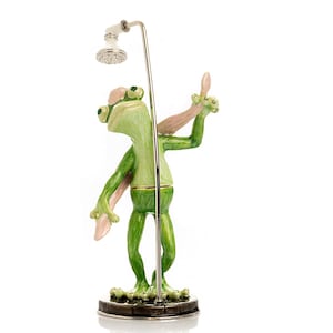 May include: A whimsical figurine of a green frog taking a shower. The frog is standing under a silver shower head, with one arm raised. The frog has pink accents and is standing on a dark, square base.