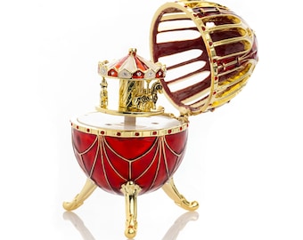 May include: A red and gold decorative egg-shaped music box with a carousel inside. The egg is open, revealing the carousel with horses and a red and white striped roof. The music box sits on three gold legs.