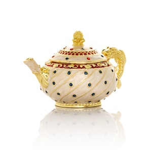 May include: A gold and white teapot with a blue and red design. The teapot has a fish-shaped handle and a decorative lid.
