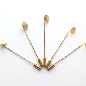 May include: Five gold-toned hat pins with round, flat, gold-toned tops. The pins are arranged in a fan shape.