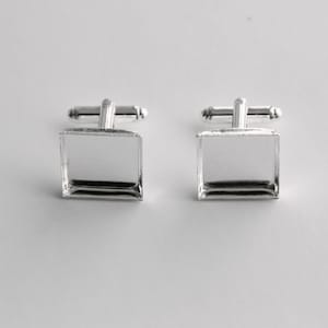 Puede incluir: Un par de gemelos de plata con inserciones de vidrio cuadradas. Los gemelos están diseñados para contener una pequeña foto u otro objeto decorativo.