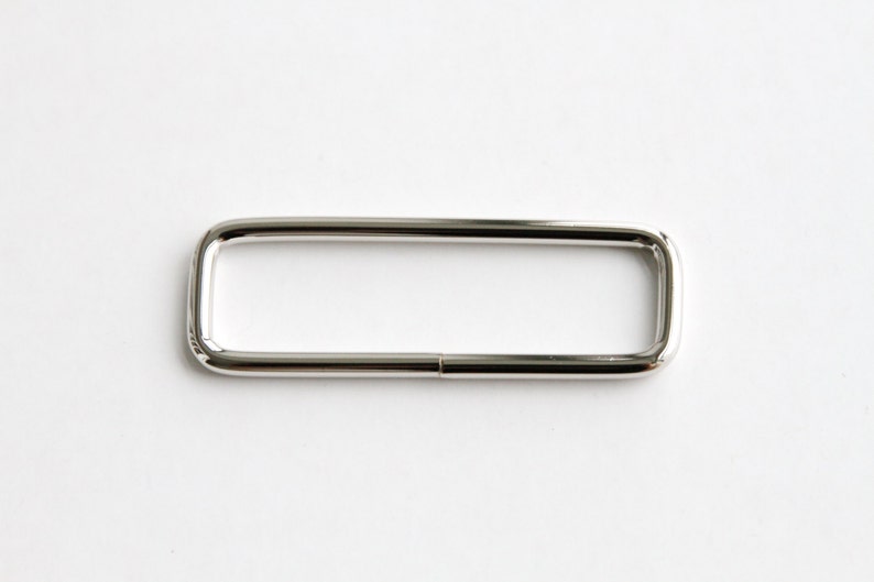 May include: A silver metal D-ring with a rectangular shape.
