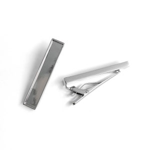 Puede incluir: Dos clips de corbata plateados. Uno es de forma simple, el otro tiene un cierre de resorte.
