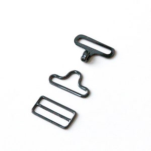 May include: Three black metal hardware pieces for sewing or crafting projects. The pieces include a slider, a hook, and a loop.