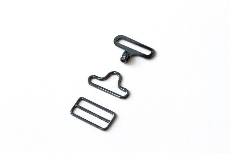 May include: Three black metal hardware pieces for sewing or crafting projects. The pieces include a slider, a hook, and a loop.