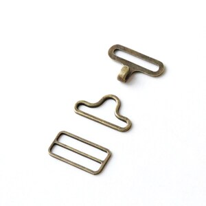 May include: Three antique gold-toned metal clasps for a garment or bag. The clasps are in the shape of a rectangle, a loop, and a hook.
