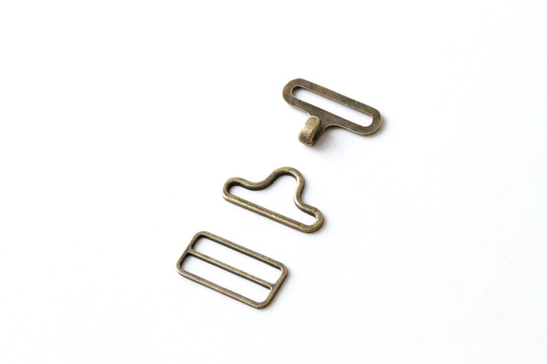 May include: Three antique gold-toned metal clasps for a garment or bag. The clasps are in the shape of a rectangle, a loop, and a hook.