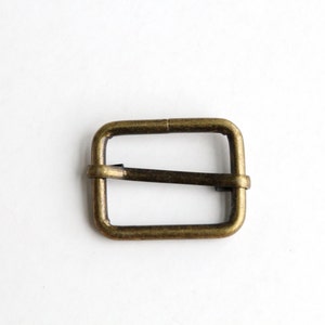 Puede incluir: Una hebilla de metal de color dorado para un cinturón o una correa.