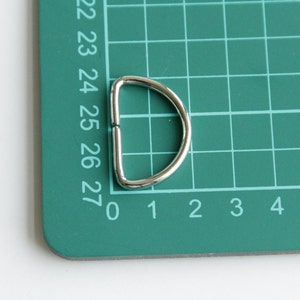 Puede incluir: Un anillo en D de metal plateado sobre una estera de corte verde con l&iacute;neas de cuadr&iacute;cula numeradas.