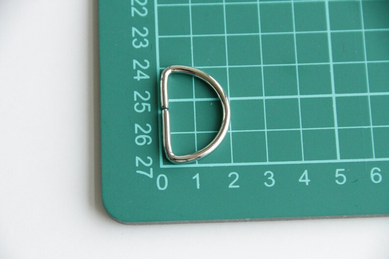 Puede incluir: Un anillo en D de metal plateado sobre una estera de corte verde con l&iacute;neas de cuadr&iacute;cula numeradas.