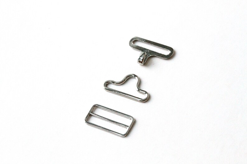 May include: Three silver metal hardware pieces for sewing or crafting projects. The pieces include a rectangular buckle, a D-ring, and a loop.
