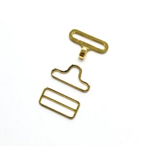 May include: Gold metal buckle set for sewing projects. The set includes a rectangular slider, a D-ring, and a hook.