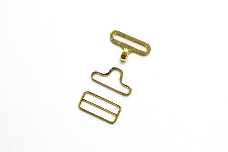 May include: Gold metal buckle set for sewing projects. The set includes a rectangular slider, a D-ring, and a hook.