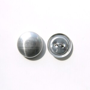 May include: A silver metal button with a smooth, shiny finish. The button has a shank on the back for sewing.
