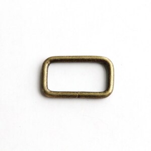 Puede incluir: Un anillo rectangular de metal dorado, también conocido como anillo en D, es una pieza de ferretería que se utiliza para sujetar correas, cadenas u otros accesorios.