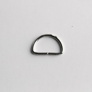 May include: A silver metal D-ring, a type of hardware used for attaching straps, chains, or other accessories.