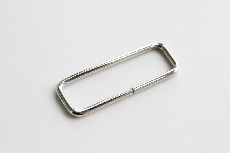 May include: A silver metal rectangular ring with a smooth finish. The ring is open on one side and has a slight bend in the middle.