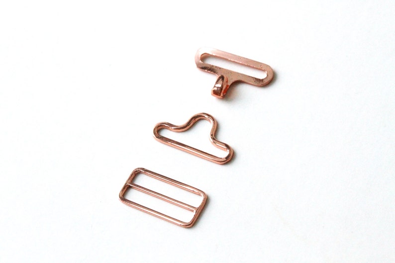 May include: Three rose gold metal clasps for sewing projects. The clasps are in different shapes, including a rectangle, a loop, and a hook.