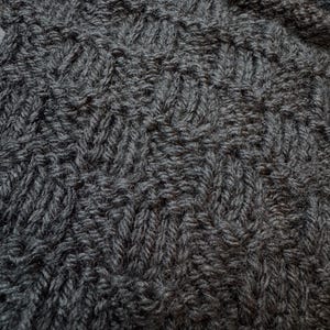Pu&ograve; includere: Un tessuto a maglia grigio antracite scuro caratterizzato da un motivo testurizzato ripetitivo di punti diagonali. Il tessuto presenta una trama densa e uniforme con anelli di filo visibili che creano una struttura geometrica in rilievo.