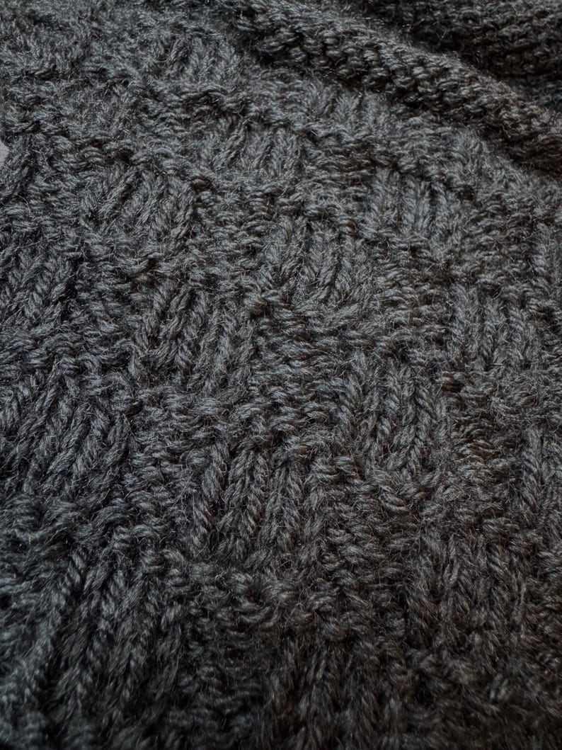 Pu&ograve; includere: Un tessuto a maglia grigio antracite scuro caratterizzato da un motivo testurizzato ripetitivo di punti diagonali. Il tessuto presenta una trama densa e uniforme con anelli di filo visibili che creano una struttura geometrica in rilievo.
