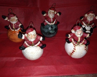 Può includere: Cinque addobbi natalizi con Babbo Natale che cavalca diverse palle da sport. Gli addobbi sono in ceramica e dipinti in rosso, bianco e verde. Le palle includono una palla da basket, una palla da bowling, una palla da calcio, una palla da baseball e una palla da golf.