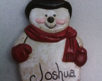 Può includere: Un ornamento a forma di pupazzo di neve bianco con un cappello nero, una sciarpa rossa e guanti rossi. Il pupazzo di neve ha un viso dipinto con guance rosate e un sorriso. L'ornamento è personalizzato con il nome "Joshua".