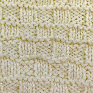 Pu&ograve; includere: Una vista ravvicinata di un tessuto lavorato a maglia color crema con un motivo a intreccio testurizzato. Il design &egrave; costituito da quadrati alternati di punti a maglia rasata verticali e punti a legaccio orizzontali, creando un effetto a griglia.
