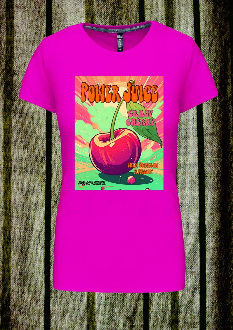 May include: A bright fuchsia short-sleeved t-shirt featuring a central graphic of a red cherry with a green leaf. The text reads POWER JUICE, CRAZY CHERRY, LACK SHALLOW A MELODY, and POWER JUICE COMPANY STOCKTON CALIFORNIA against a colorful background.