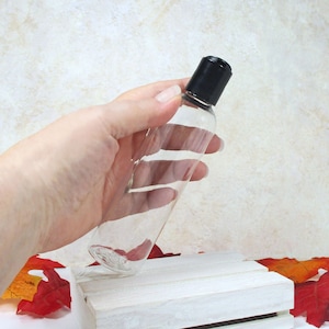 May include: A clear plastic bottle with a black cap. The bottle is empty and is being held by a hand.