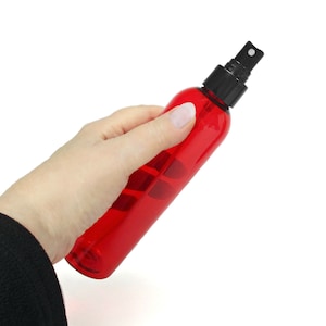 May include: A red plastic spray bottle with a black spray nozzle. The bottle is being held in a hand.