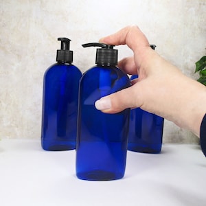 May include: Three blue plastic pump bottles with black pumps. The bottles are filled with a clear liquid. A hand is pressing down on the pump of one of the bottles.