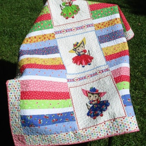 May include: A colorful quilt with a striped pattern and three appliqued images of kittens wearing hats. The quilt is made with a variety of fabrics in shades of pink, red, blue, green, and yellow.